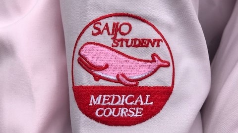 医療系「Student Assistant（スチューデント・アシスタント）」オリジナルロゴです。 
「ピンクのくじら🐬」がサポート学生の腕に乗っています！