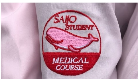 医療系「Student Assistant（スチューデント・アシスタント）」オリジナルロゴです。 
「ピンクのくじら🐬」がサポート学生の腕に乗っています！
この活動を立ち上げた先輩のデザインです！
